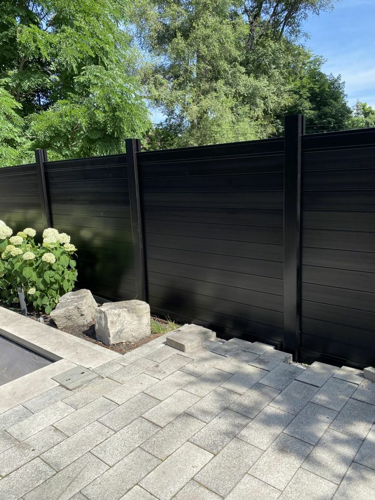 a large black fence next to a brick walkway in front of some trees and bushes