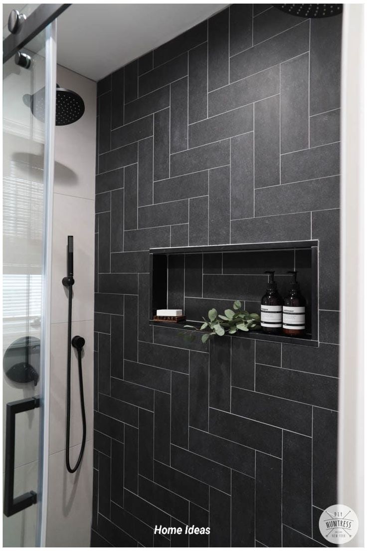 a black tiled bathroom with shelves on the wall and shower head in the corner next to it