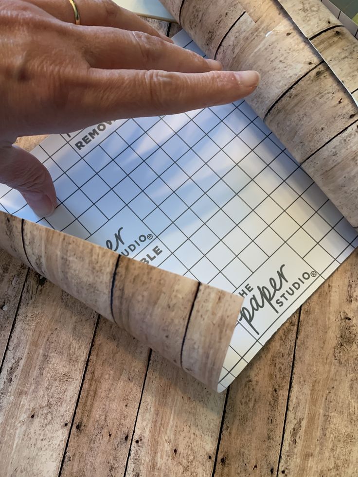 a person's hand pointing at a piece of paper on top of a wooden table