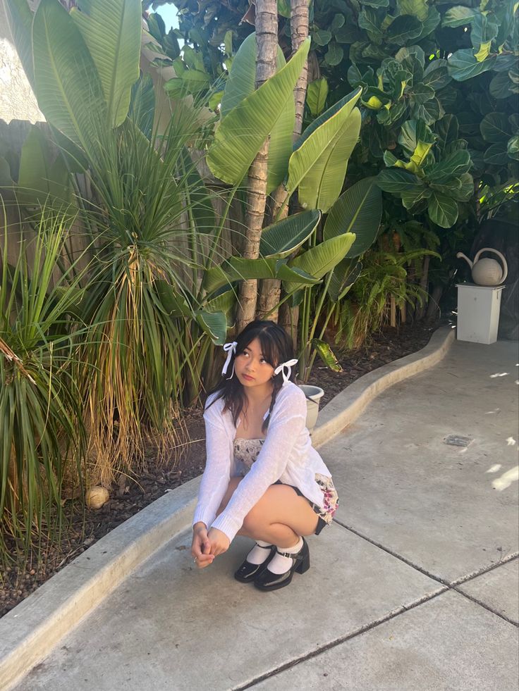 a woman kneeling down on the ground in front of some trees and plants with her legs crossed