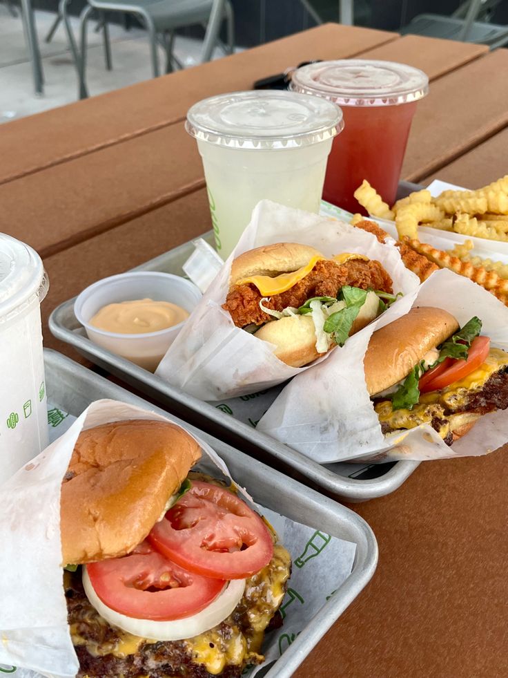 two trays filled with sandwiches and fries next to drinks