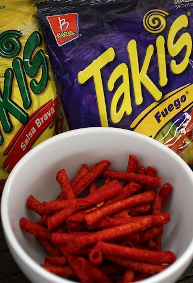 two bags of taks and a white bowl filled with red cheetos sitting next to each other