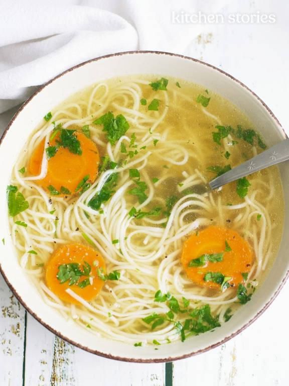 a bowl of soup with noodles, carrots and parsley