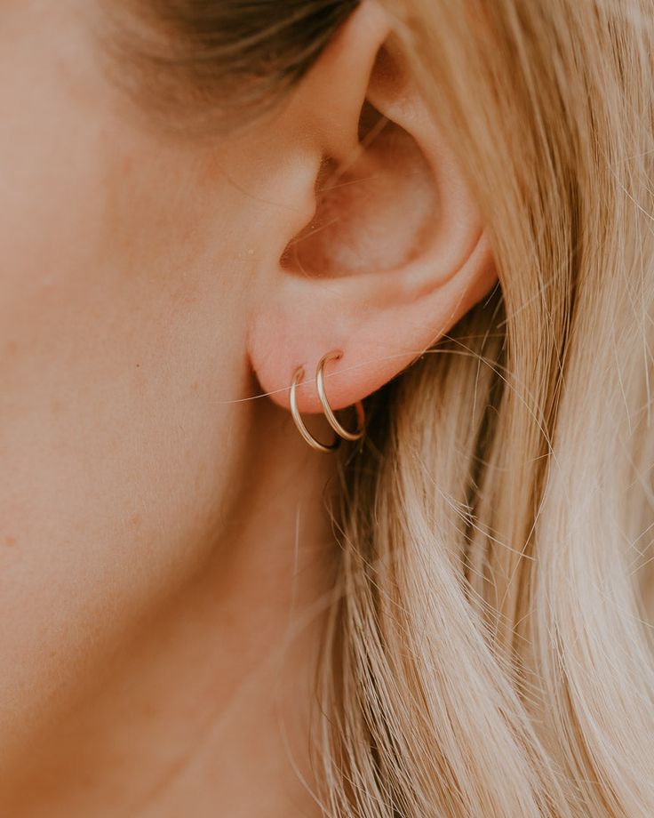 a woman with blonde hair wearing gold hoop earrings and a white top is looking down at her ear