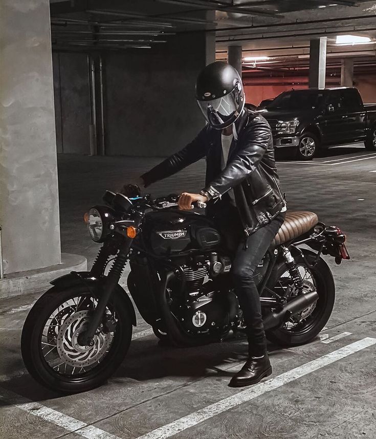 a man sitting on a motorcycle in a parking lot wearing a leather jacket and helmet