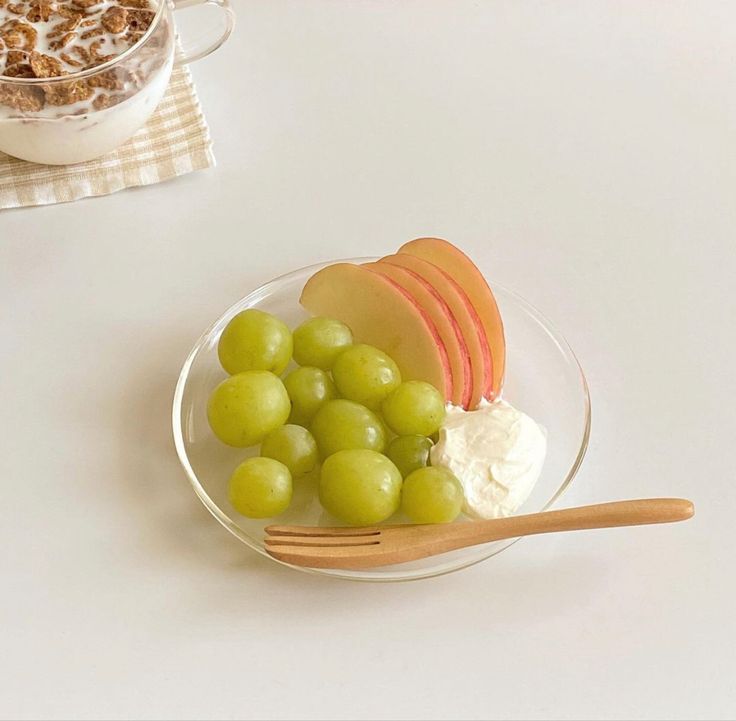 a plate with grapes, apples and yogurt on it next to a bowl of granola