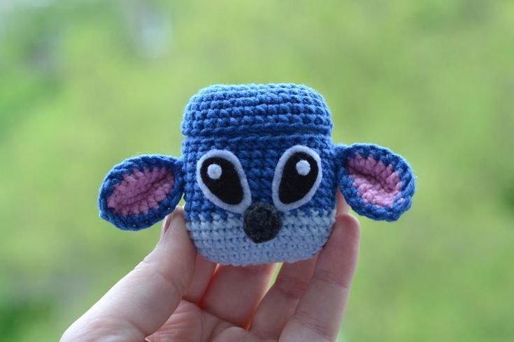 a small crocheted animal with eyes and ears is held up in front of the camera