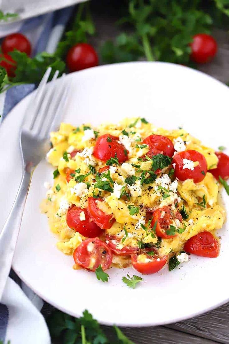 an omelet with tomatoes, cheese and parsley on a white plate next to a fork