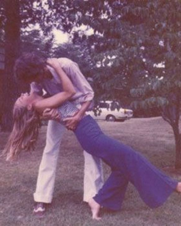 a man and woman are kissing in the grass with trees in the back ground behind them