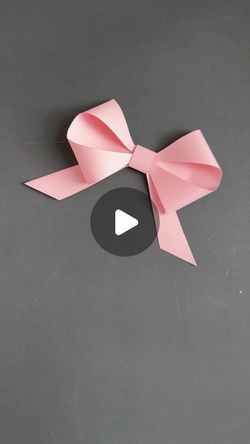 an origami bow with a play button in the middle on a gray surface