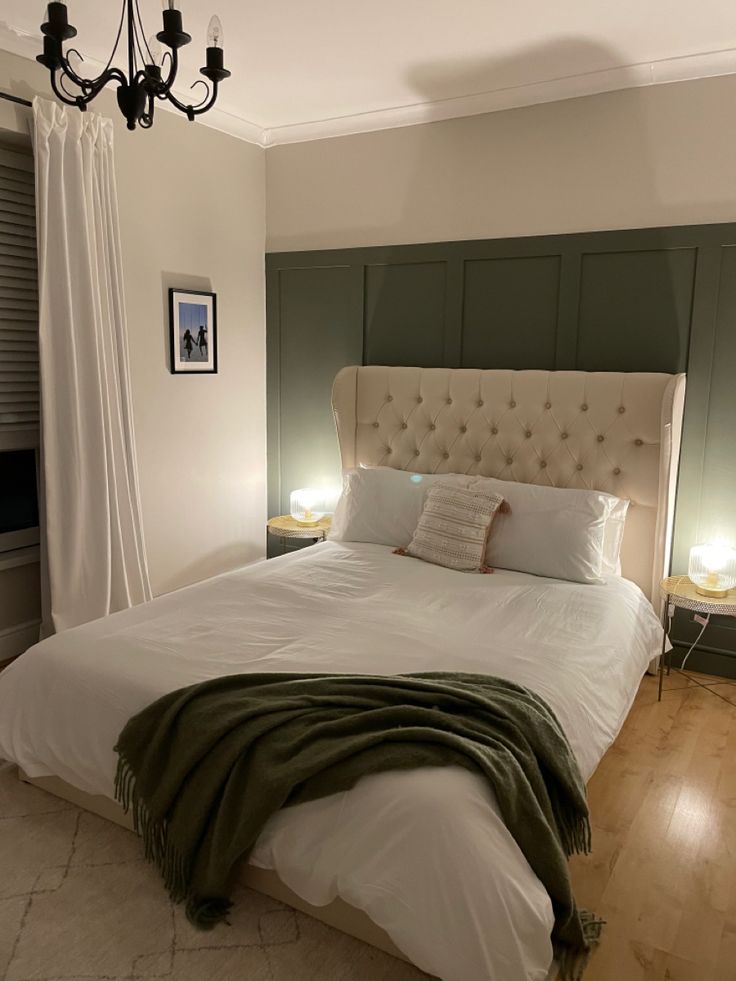 a bed with white sheets and pillows in a bedroom next to a chandelier