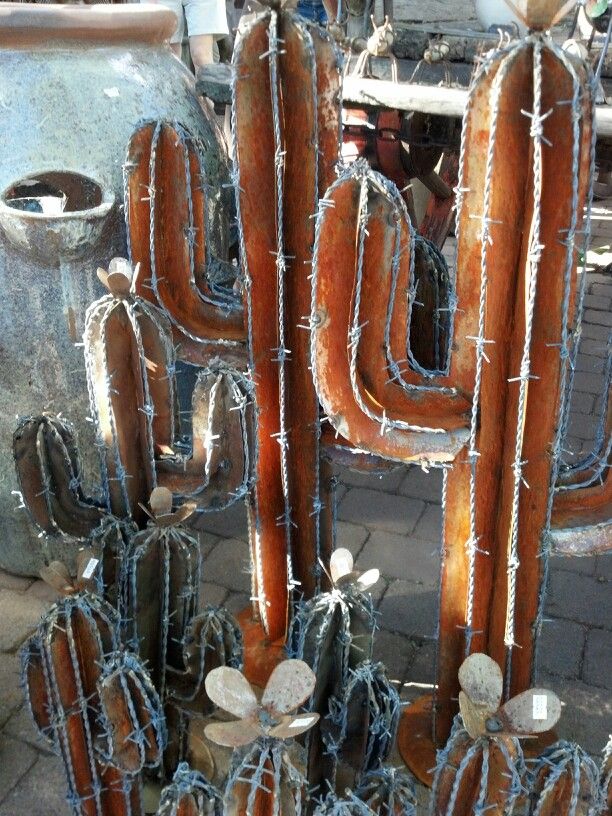 a large group of metal cactus sculptures sitting on top of a brick floor next to a building