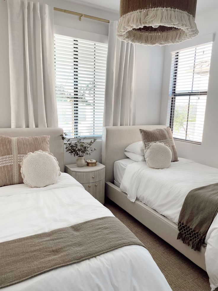 two beds in a bedroom with white sheets and brown pillows, one has a light fixture hanging from the ceiling