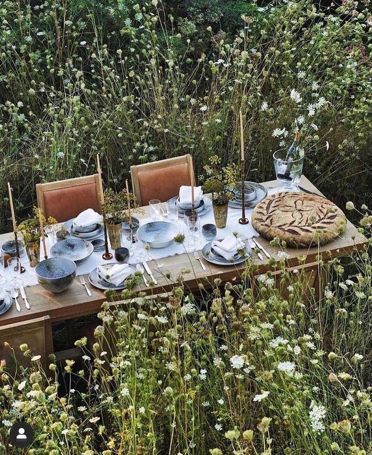 an outdoor table set with plates and silverware in the middle of tall grass, surrounded by wildflowers