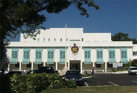 a white building with blue shutters and cars parked in front