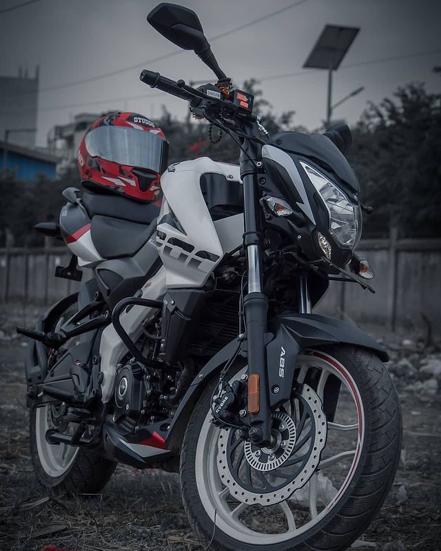 a white and black motorcycle parked on top of a dirt field next to a fence