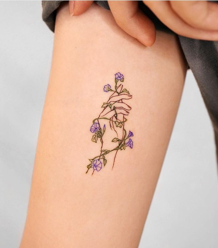 a woman's arm with a tattoo on it that has purple flowers growing out of it