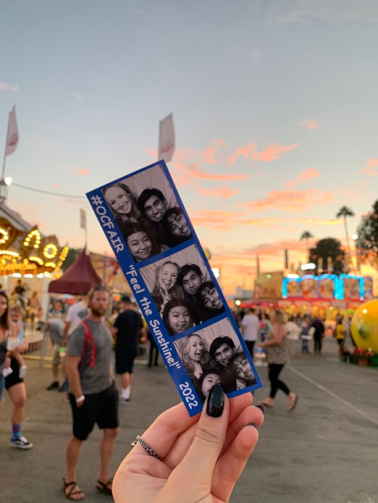 a person holding up a ticket with photos on it at an amusement park during the day