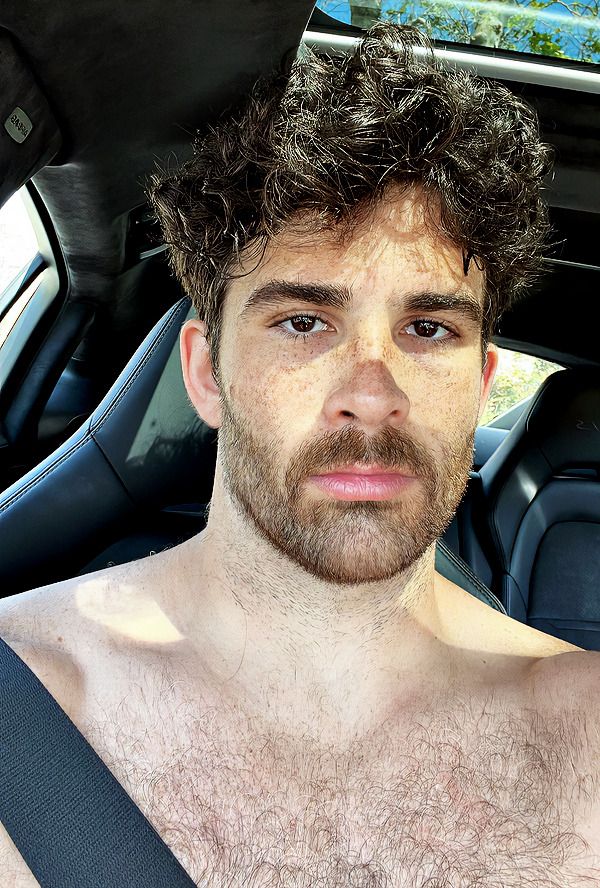 a shirtless man sitting in the back seat of a car looking at the camera