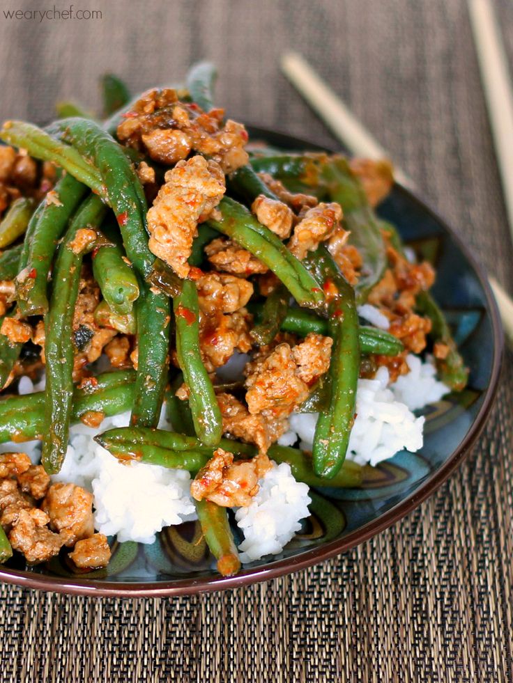 a plate filled with green beans and rice on top of a table next to chopsticks