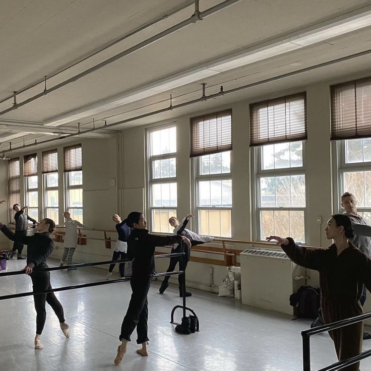 several people are practicing ballet in an empty room with large windows and sun shining through the windows