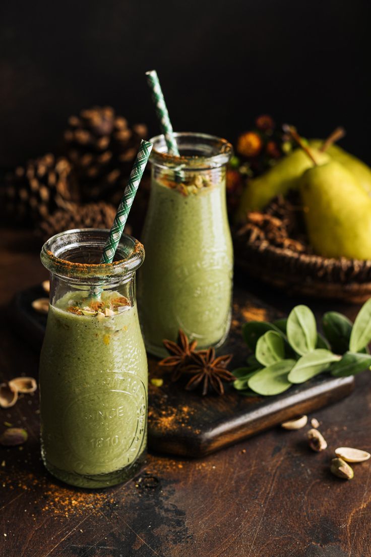 two glasses filled with green smoothie on top of a wooden table