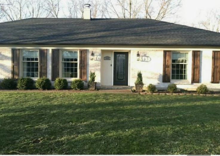 a small white house with brown shutters and green grass in front of the door