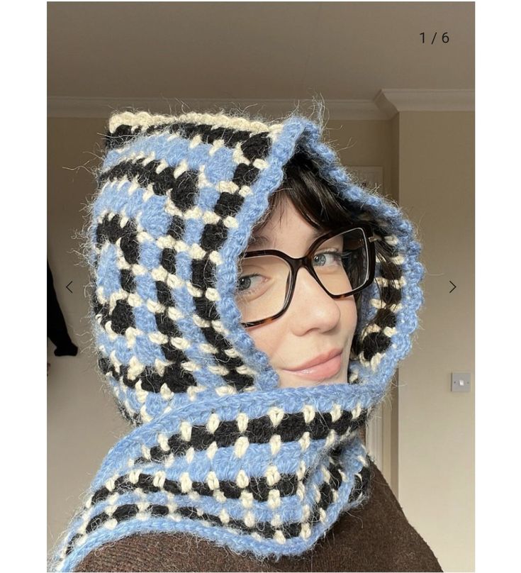 a woman wearing glasses and a knitted scarf with hood on her head is looking at the camera