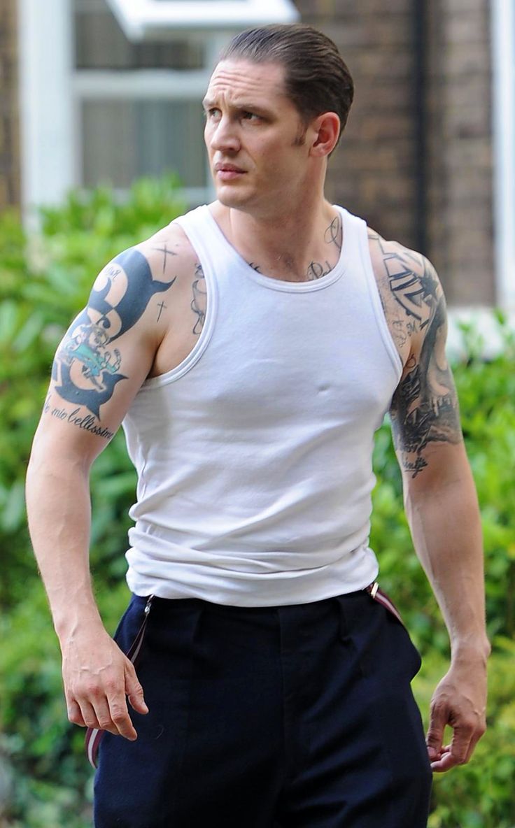 a man with tattoos on his arms and chest walking down the street in front of a house