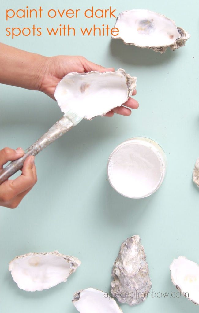 a person holding a spoon over some oysters on a blue surface with text that reads paint over dark spots with white