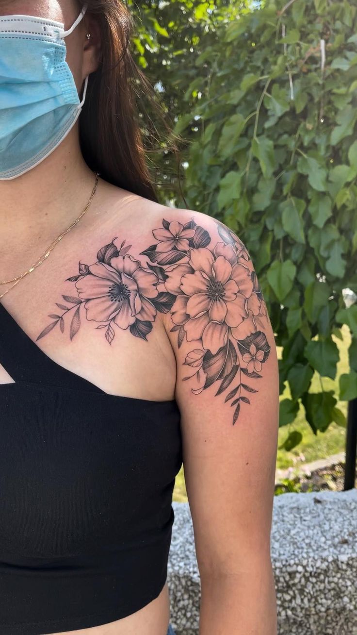 a woman wearing a face mask with flowers on her shoulder and chest tattoo design in black ink