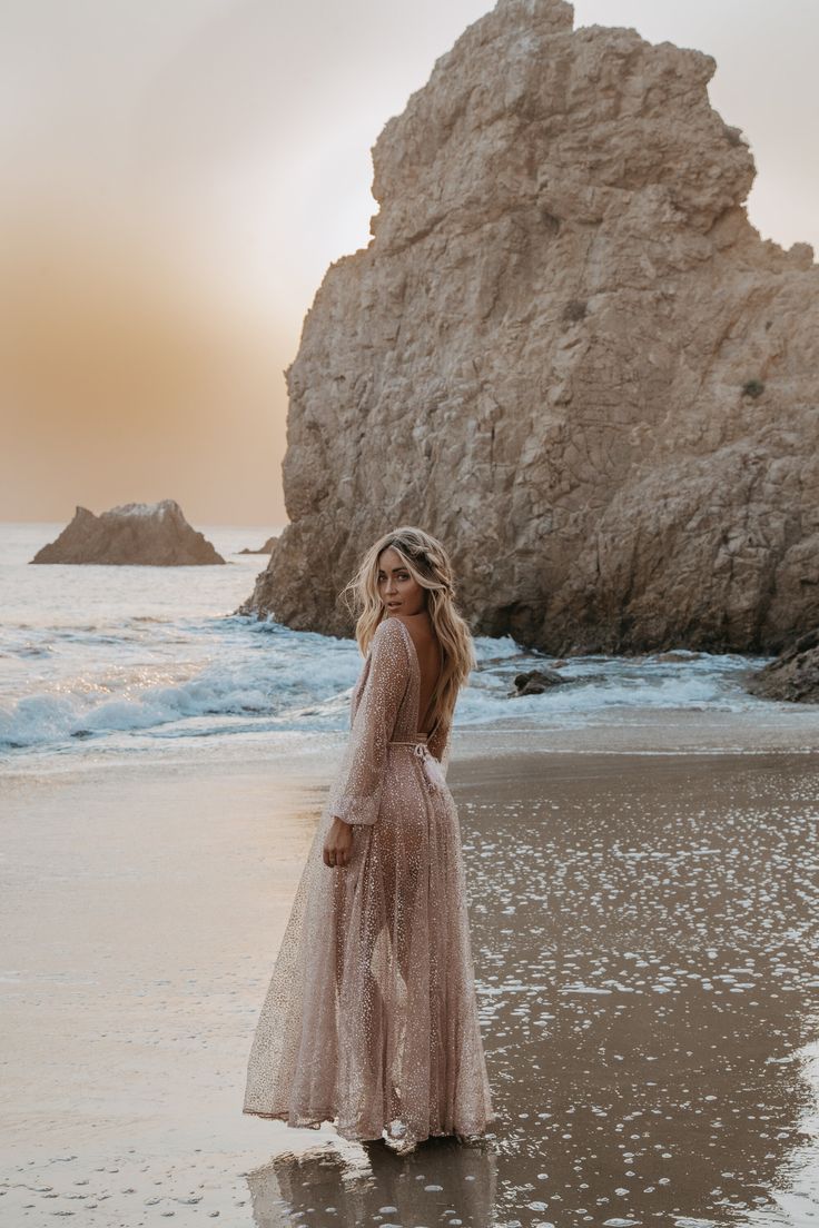 a woman standing on top of a sandy beach next to the ocean wearing a dress