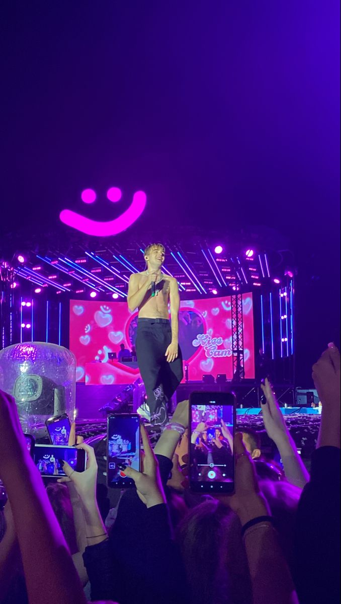 a man standing on top of a stage surrounded by people holding up their cell phones