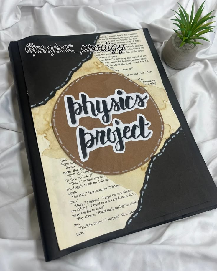 an open book with the words physics project on it next to a potted plant