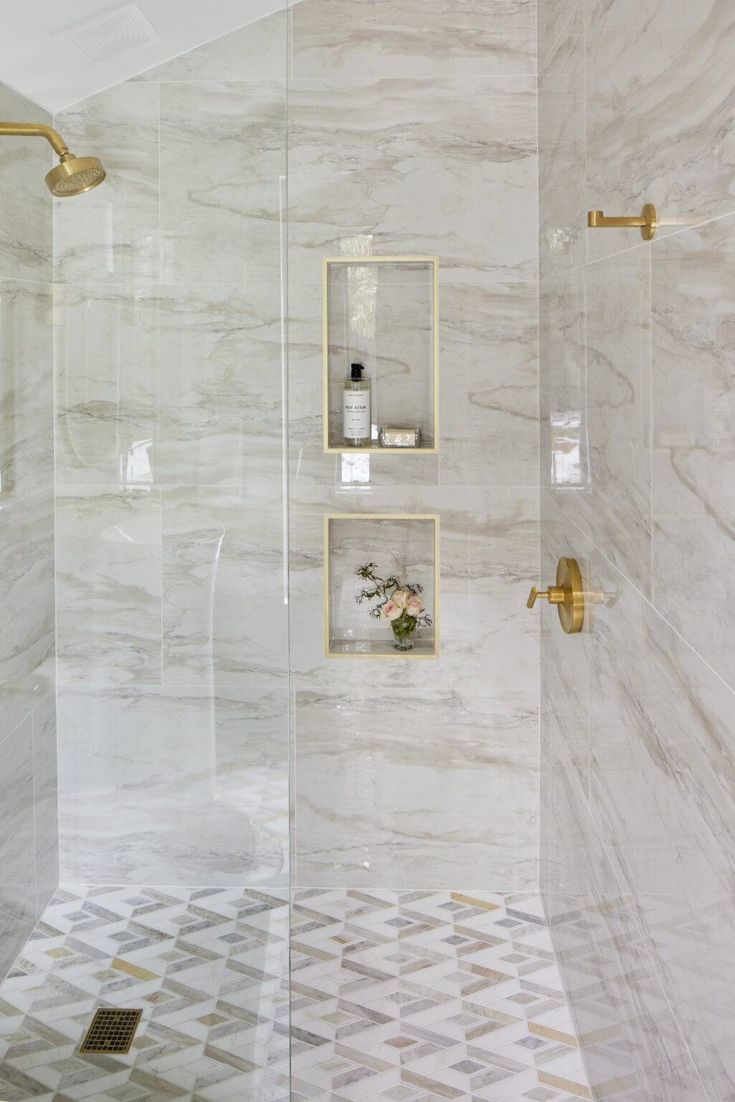 a bathroom with white marble walls and gold fixtures on the shower wall, along with a tiled floor