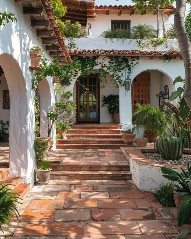 a white house with lots of plants on the front and side steps leading up to it