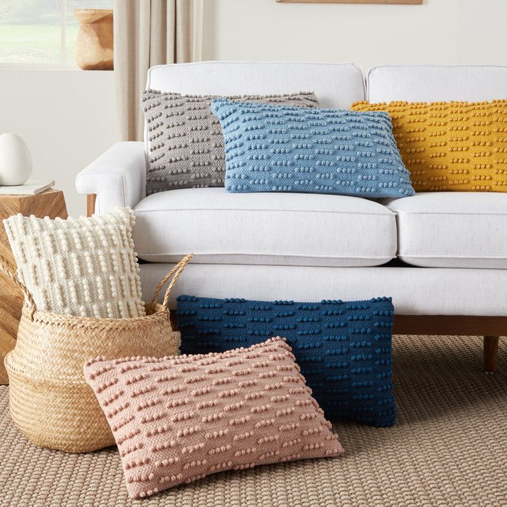 four different colored pillows sitting on the floor next to a white couch in a living room