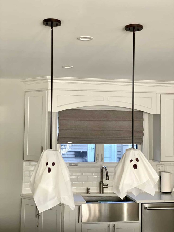 two white ghost heads hanging from the ceiling in a kitchen with stainless steel sink and dishwasher