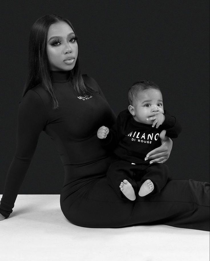 a woman holding a baby while sitting on top of a white floor next to a black wall