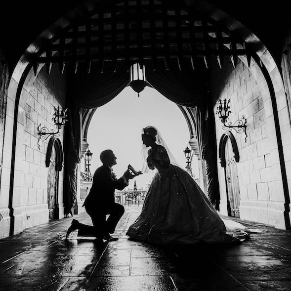 a man kneeling down next to a woman in a wedding dress under an arch on the ground