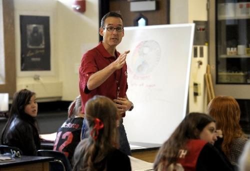 a man standing in front of a whiteboard giving a presentation to children sitting at desks