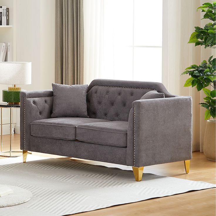 a gray couch sitting on top of a wooden floor next to a lamp and window