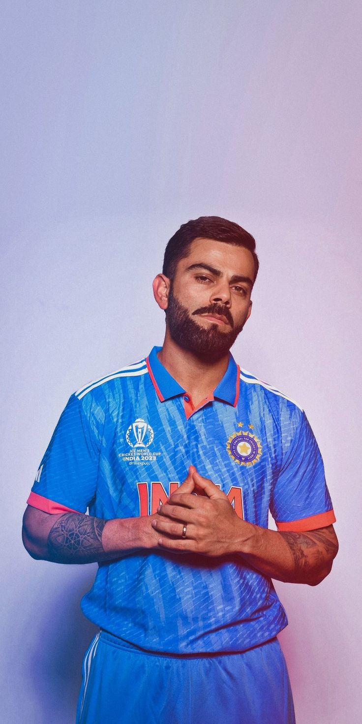 a man with a beard and tattoos standing in front of a white wall wearing a blue shirt