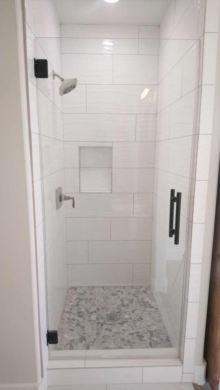 a walk in shower sitting next to a white tiled wall and floor with black handles