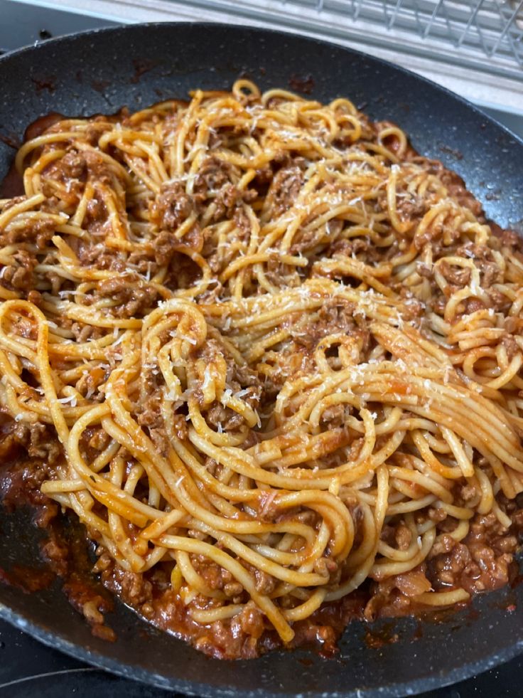 a skillet filled with spaghetti and meat on top of a stove burner oven