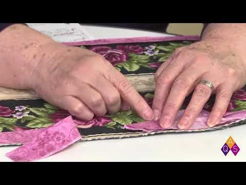 two hands on top of a piece of fabric with pink flowers and green leaves around it