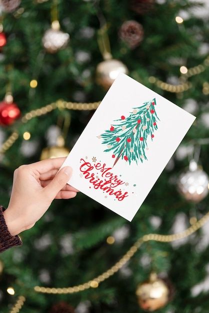 a person holding up a christmas card in front of a christmas tree