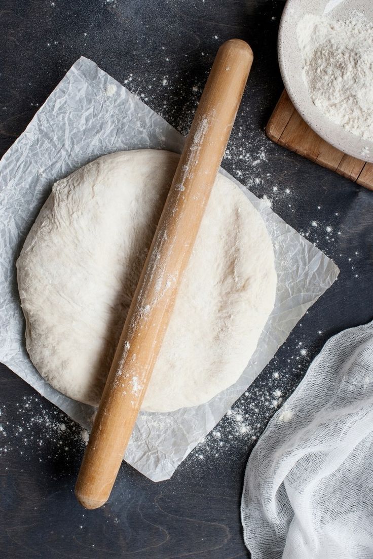 a wooden rolling pin sitting on top of a table next to flour and a loaf of bread