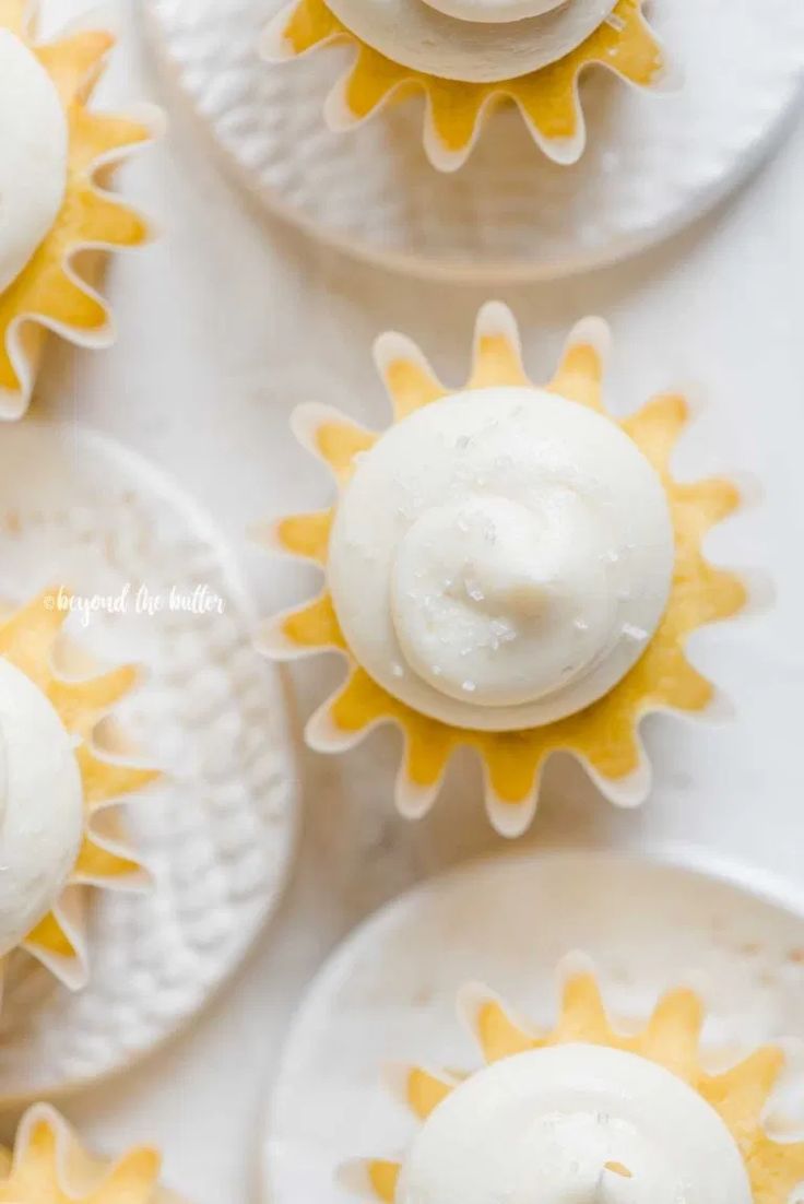 four cupcakes with frosting and sun decorations on them sitting on white plates