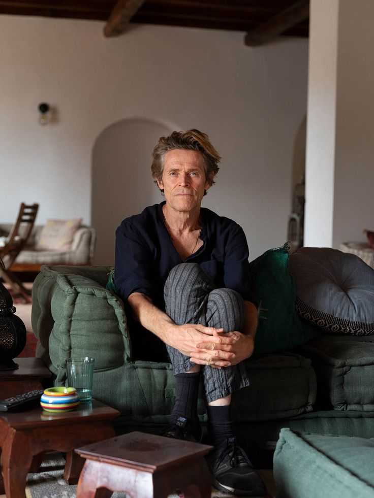 a man sitting on top of a green couch in a living room next to a coffee table